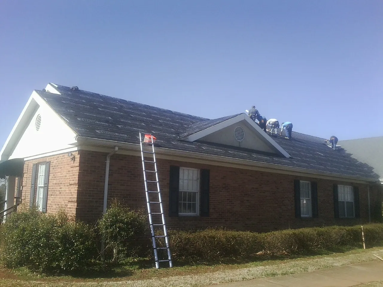 Crew tearing shingles off a brick ranch roof with a ladder set — Emergency Roof Repair work by our crew in Dundee