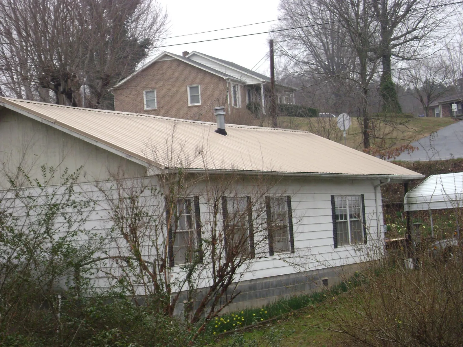 Tan metal roof on a white sided house set into a hillside — Commercial Roofing by Roofing Brothers in Dundee